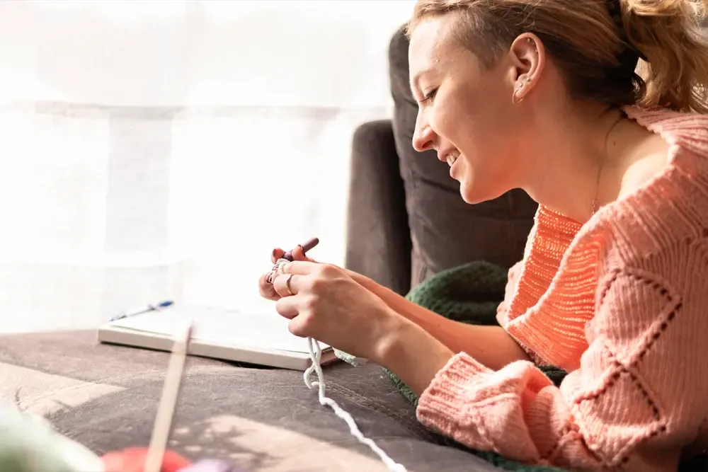 A smiling woman engaged in therapeutic knitting activity, promoting creative expression and relaxation at a drug and alcohol detox center in Nashville.