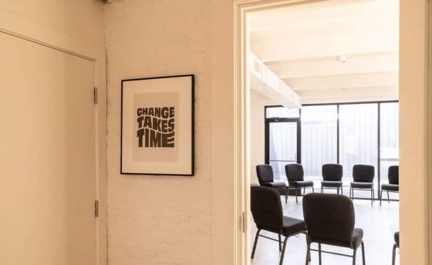 A motivational wall art reading "Change Takes Time" at a drug and alcohol rehab center in Louisville, KY, next to a group therapy room with arranged chairs.