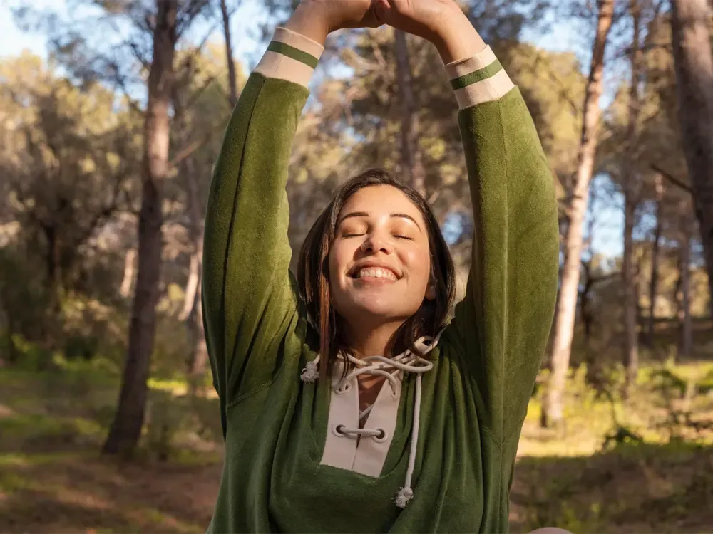 A joyful woman stretches in a serene forest setting, symbolizing the renewal and recovery offered by a drug and alcohol detox center in Nashville.